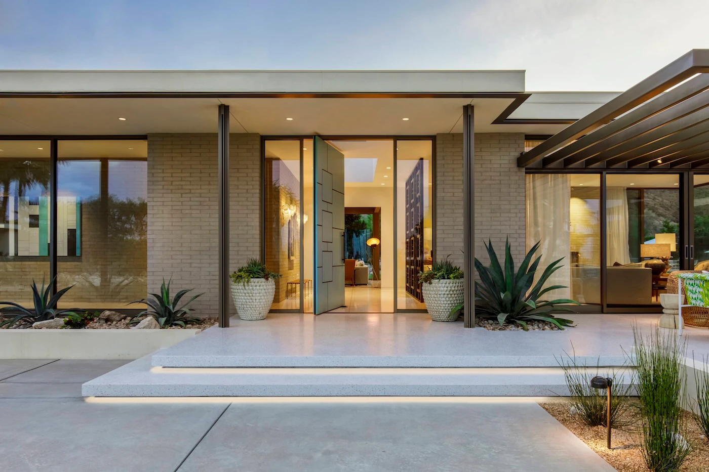Open contemporary pivot entry door framed by glazing and light brickwork.